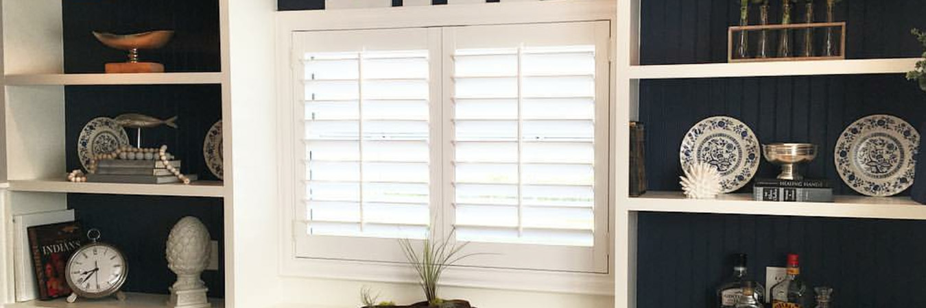 white plantation shutters covering a small window flanked with bookcases
