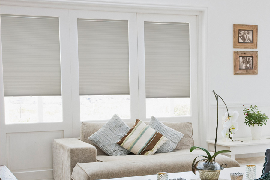  Light gray cellular shades on three separate windows in large light wood and beige colored living room.