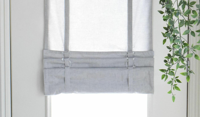 With a tiered tumble shade in New York, you can block sun glare all year round. Gray rolled tumble shade on a glass door