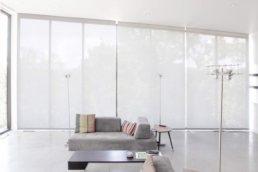 Motorized window shades make controlling natural light effortless in your New York great room. White motorized shades on a wall of tall great room windows
