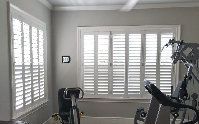 Draft-blocking window coverings are especially important in rooms with windows on more than one wall. New York home gym with shuttered windows.