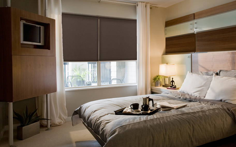 Blackout roller shades can help you fall asleep comfortably. Dark roller shakes in a modern bedroom.