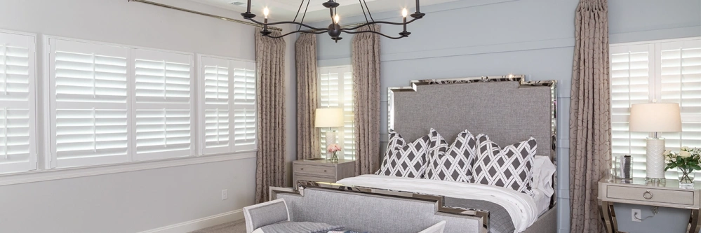White Polywood shutters and gray curtains on bedroom windows of different sizes